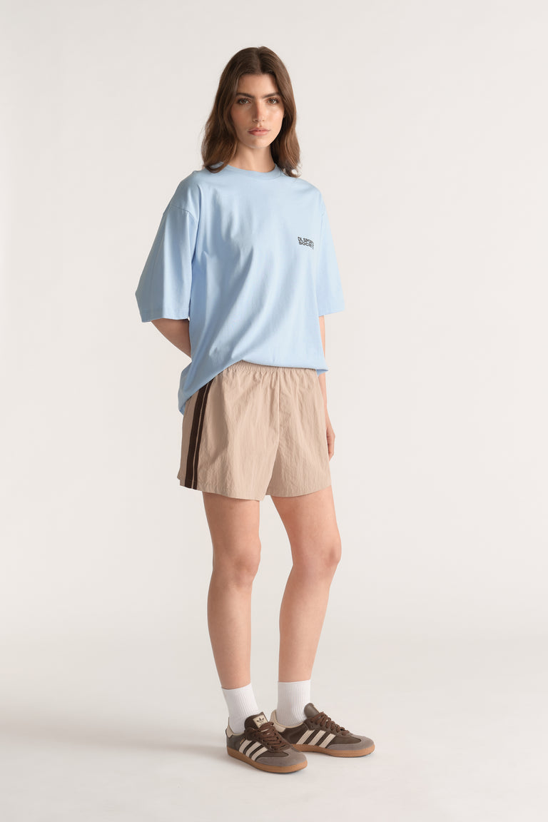 Woman wearing beige shorts with dark side stripes, a light blue tee and brown sneakers