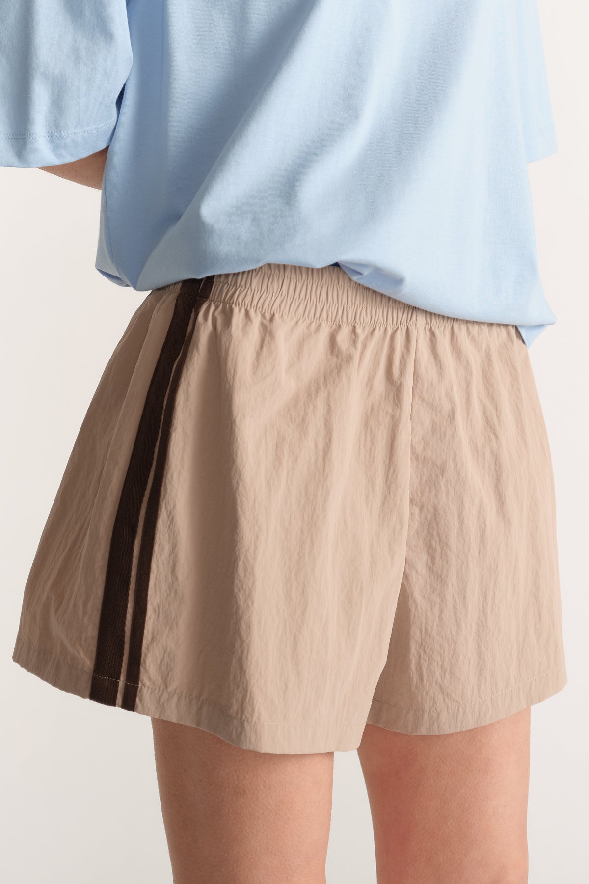 Woman wearing beige elastic waist shorts with a dark side stripe and a light blue oversized top
