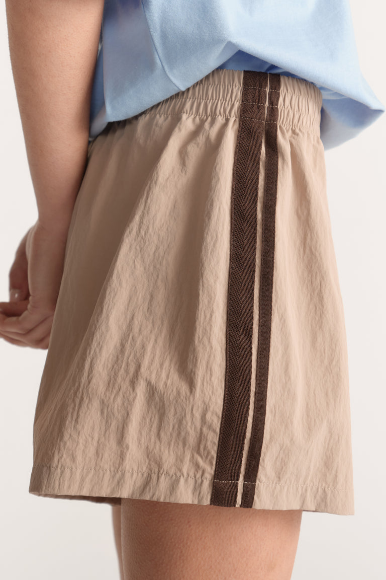 Beige mid rise shorts with an elastic waist and dark brown side stripe worn with a light blue top