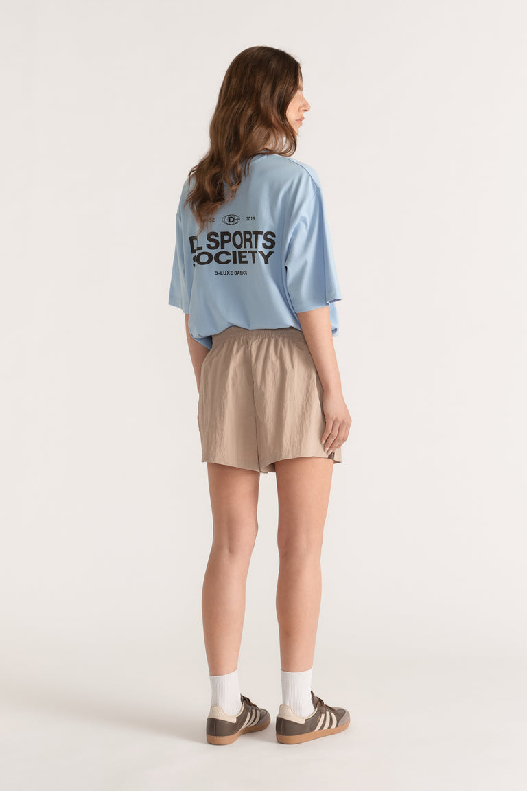 Woman wearing beige elastic waist shorts with a blue oversized tee, white socks and brown sneakers