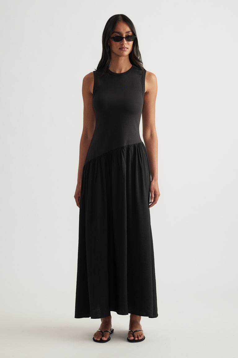 Model wearing a black sleeveless maxi dress with a fitted bodice and flowing skirt, styled with sunglasses and sandals