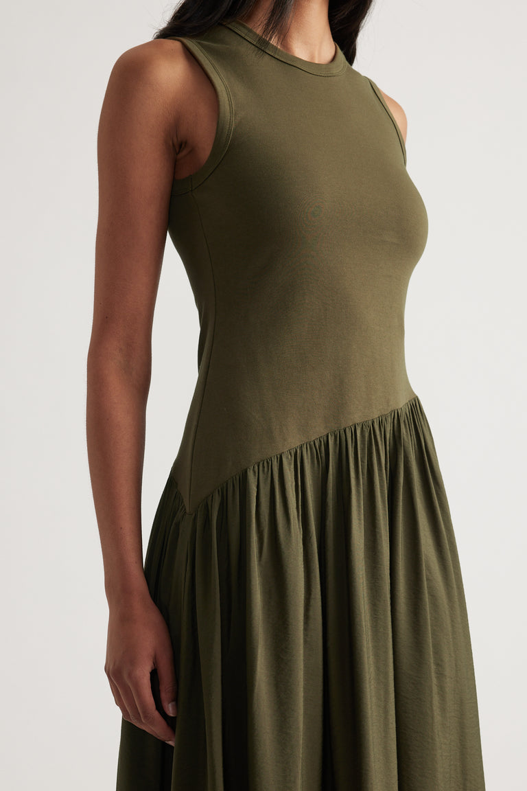 Woman wearing an olive green sleeveless maxi dress with a crew neckline and asymmetric gathered skirt