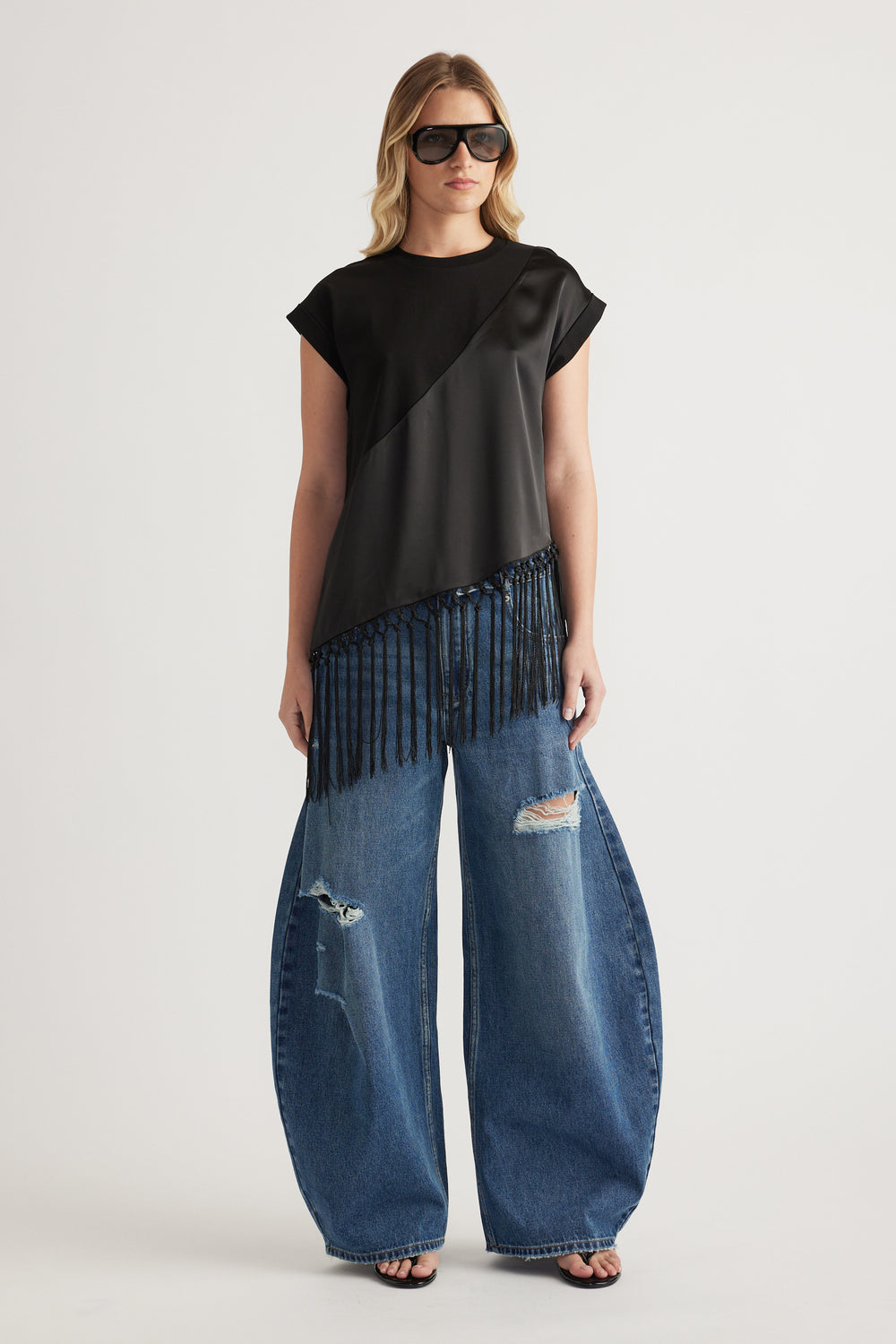 Woman wearing a black fringe hem tee with wide leg distressed jeans and sunglasses