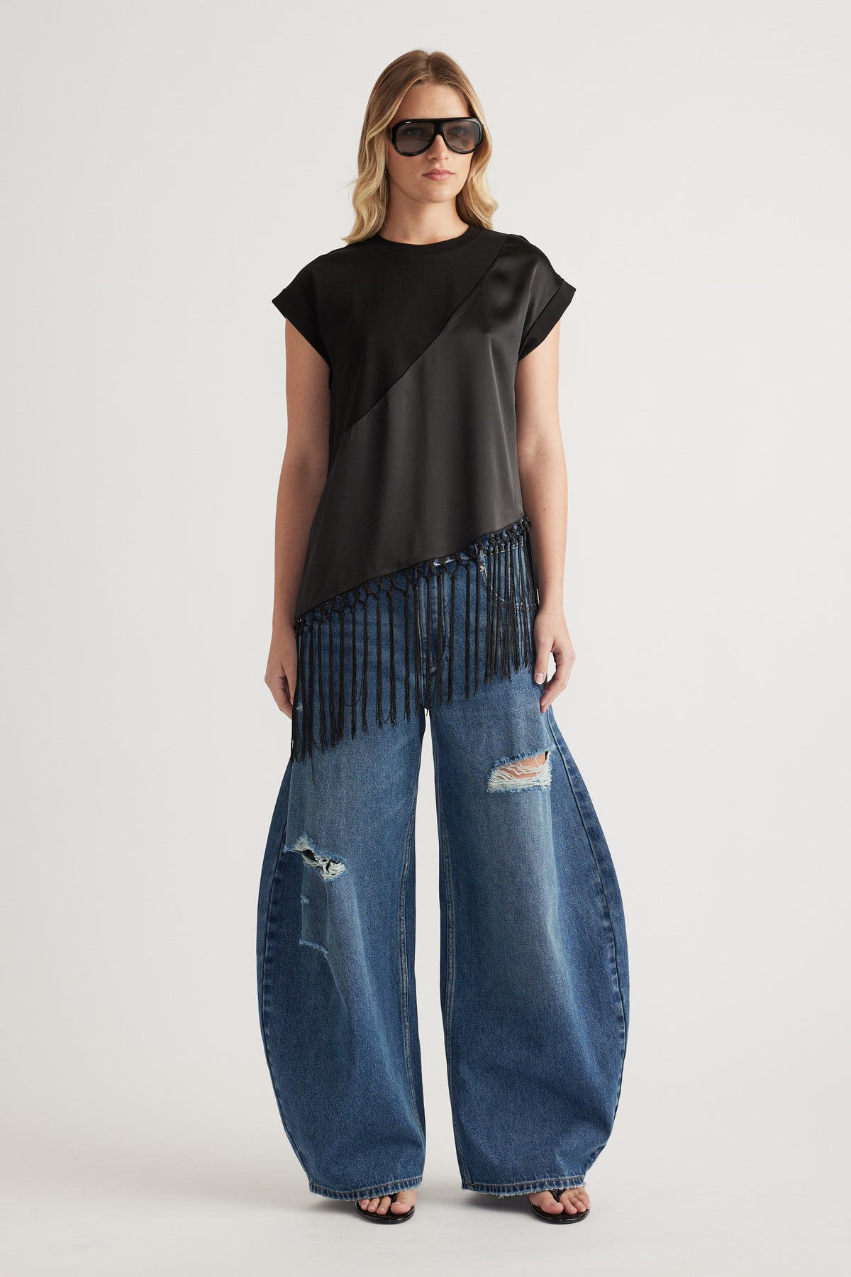 Woman wearing a black fringe hem tee with wide leg distressed jeans and sunglasses