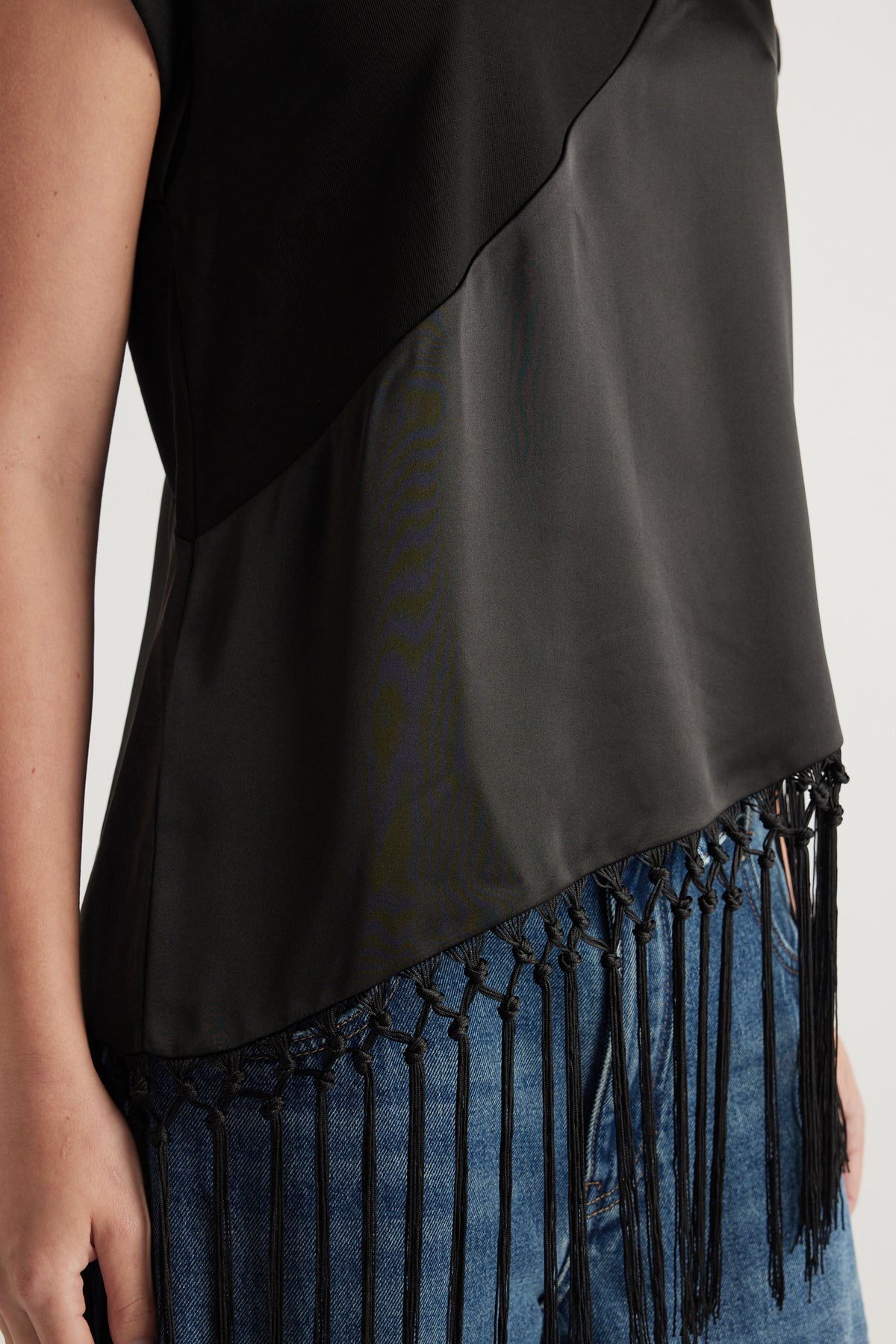 Close-up of a woman wearing a black satin tee with an asymmetric fringe hem over blue jeans