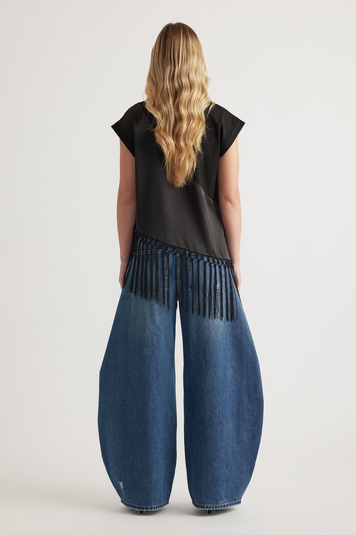 Woman wearing a black fringe hem tee with wide leg blue jeans, viewed from behind