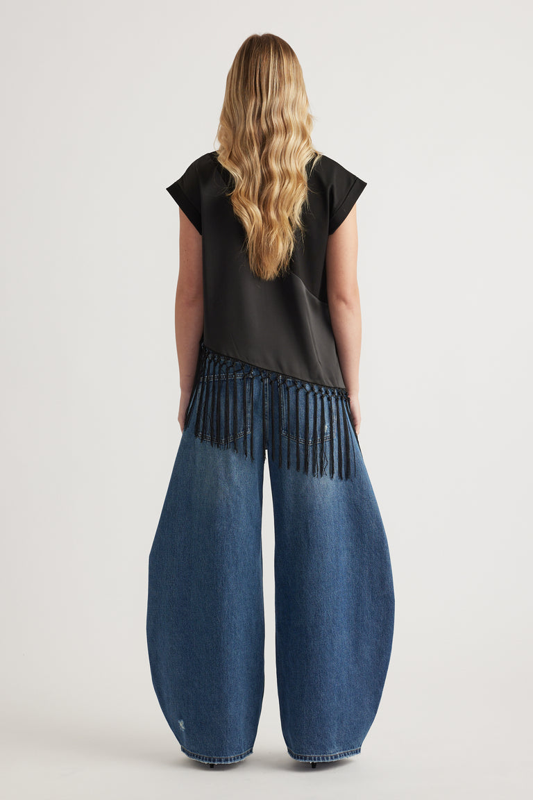 Woman wearing a black fringe hem tee with wide leg blue jeans, viewed from behind