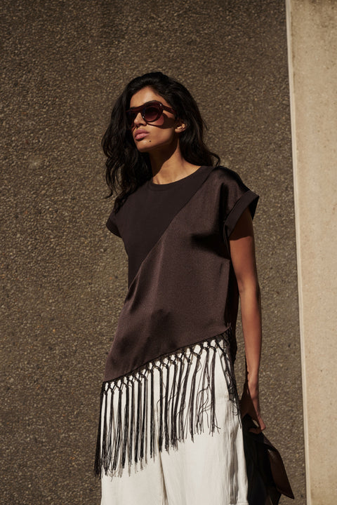 Woman wearing a dark satin fringe hem tee with white pants and sunglasses