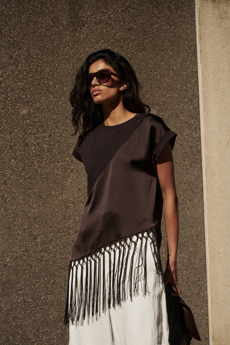 Woman wearing a dark satin fringe hem tee with white pants and sunglasses