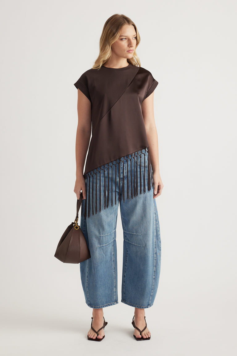 Woman wearing a dark brown satin tee with an asymmetric fringe hem, relaxed blue jeans and sandals
