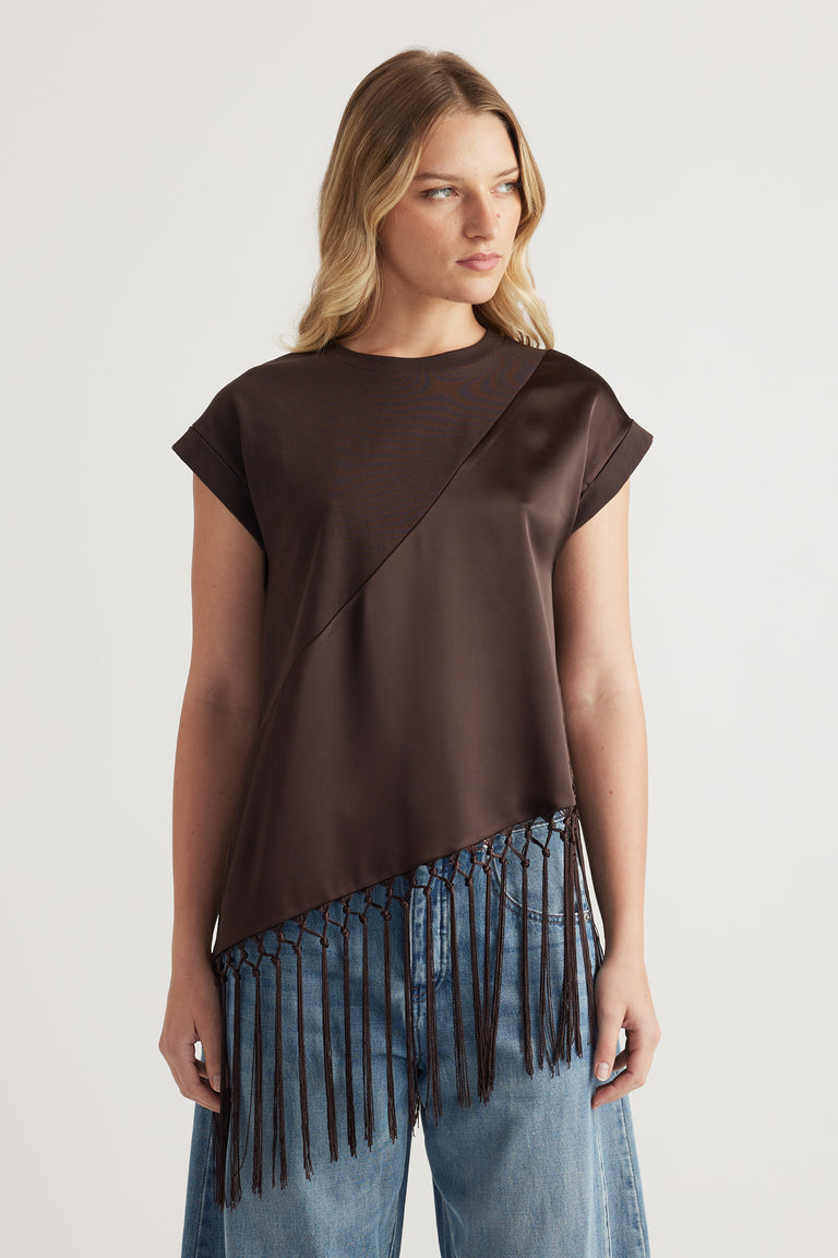 Woman wearing a dark brown asymmetric satin tee with a fringe hem and light wash jeans