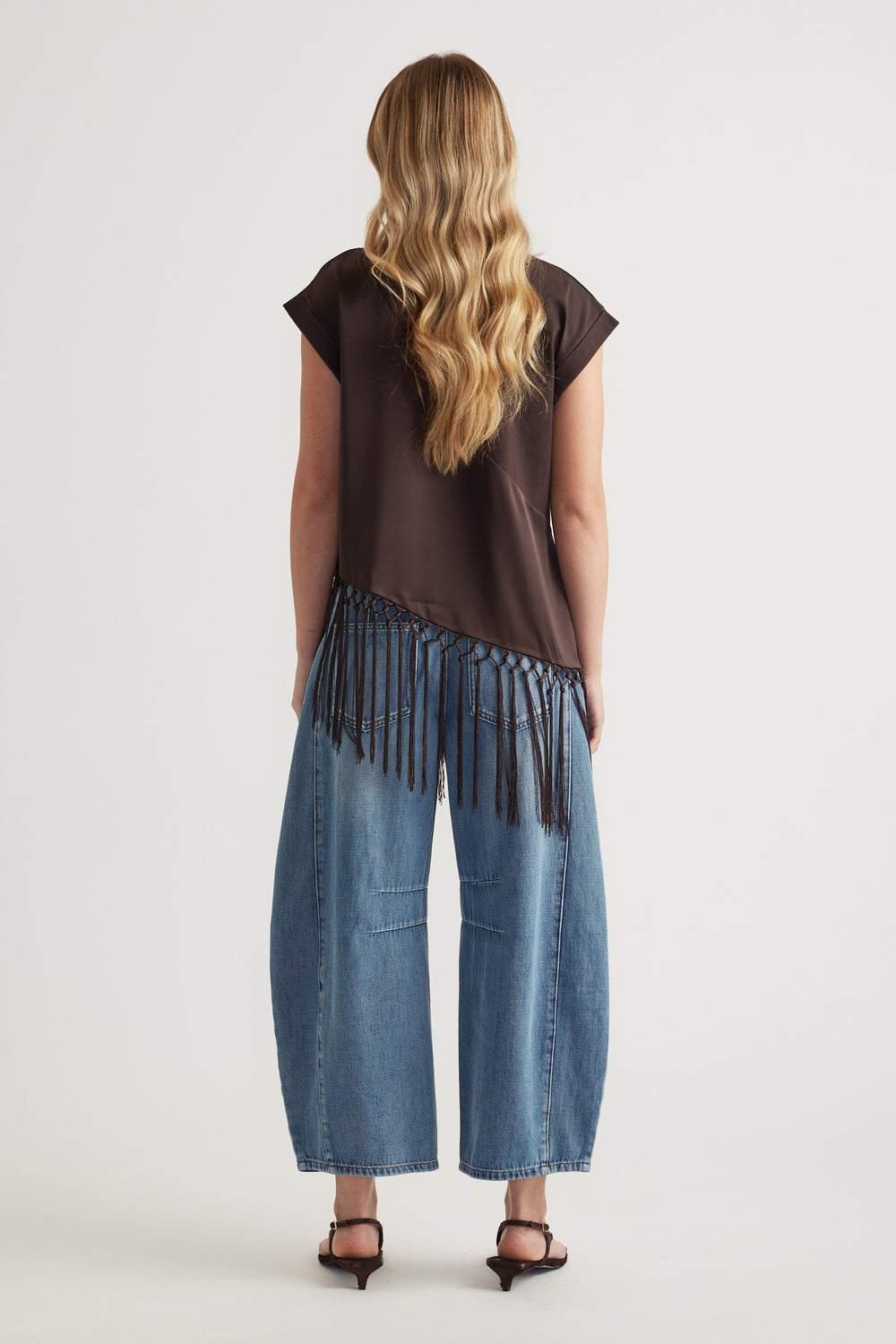Woman wearing a dark brown satin tee with a fringe hem and wide leg blue jeans