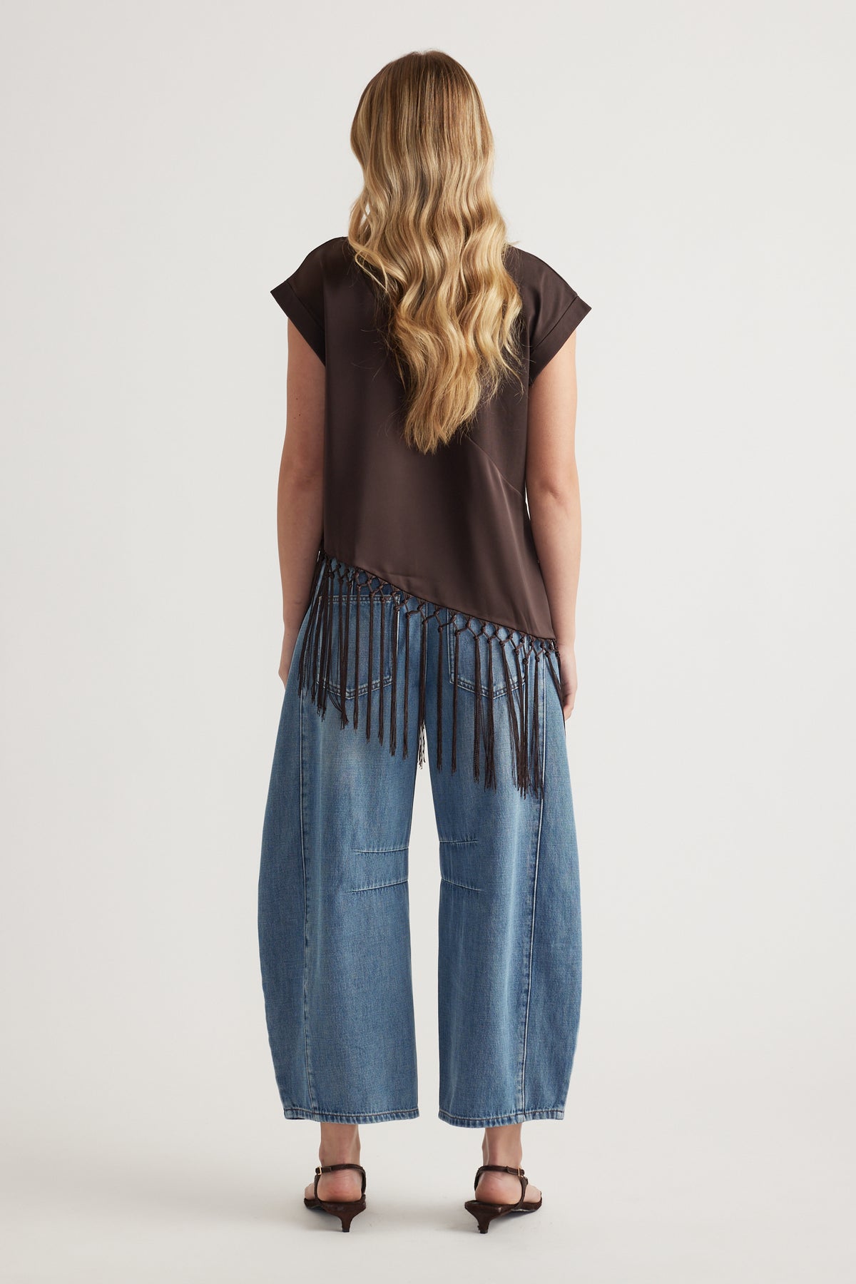 Woman wearing a dark brown satin tee with a fringe hem and wide leg blue jeans