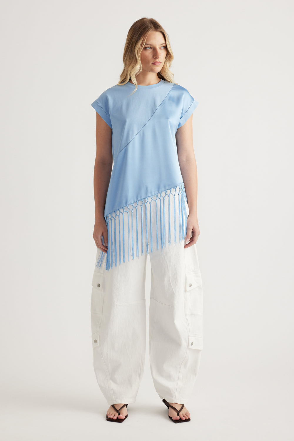 Woman wearing a light blue tee with an asymmetric fringe hem, white cargo pants and sandals