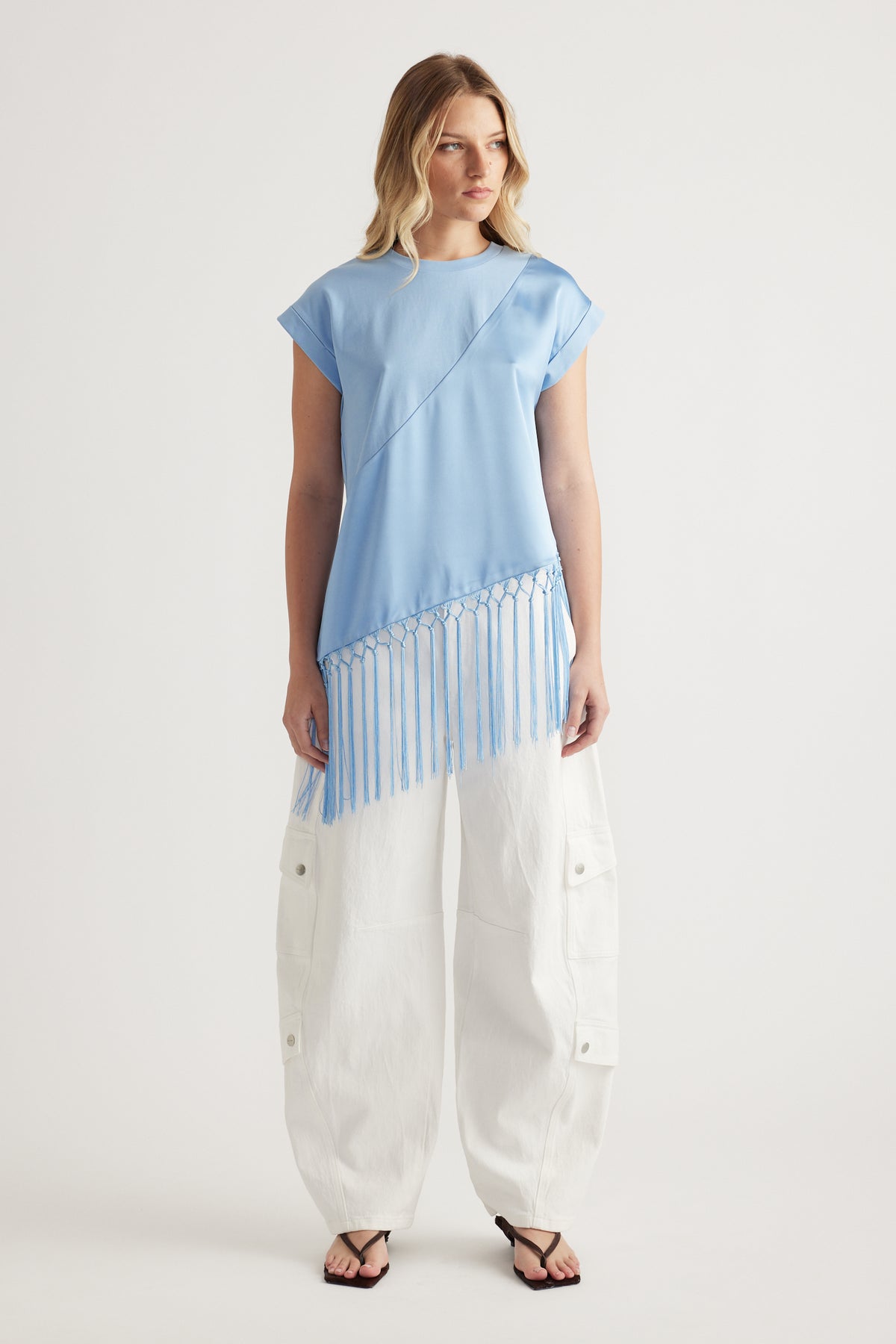 Woman wearing a light blue tee with an asymmetric fringe hem, white cargo pants and sandals
