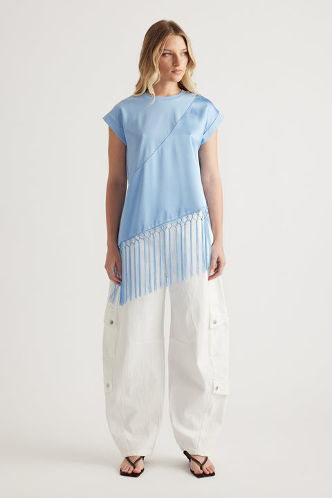 Woman wearing a light blue tee with an asymmetric fringe hem, white cargo pants and sandals