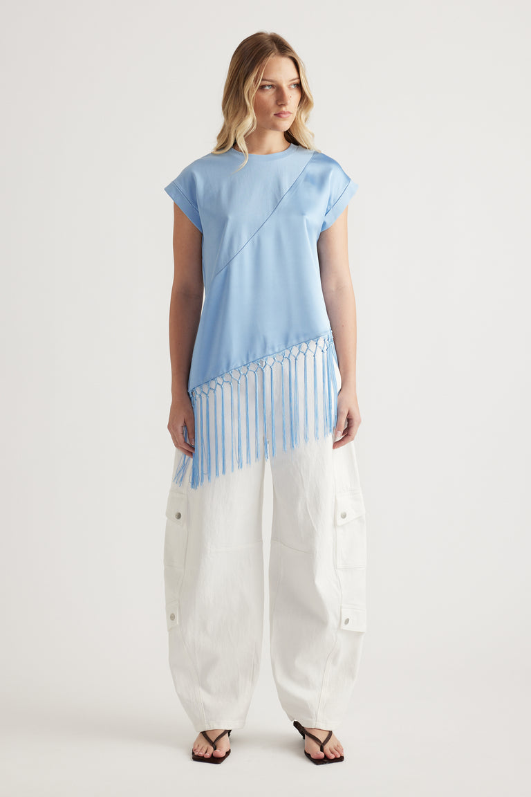 Woman wearing a light blue tee with an asymmetric fringe hem, white cargo pants and sandals