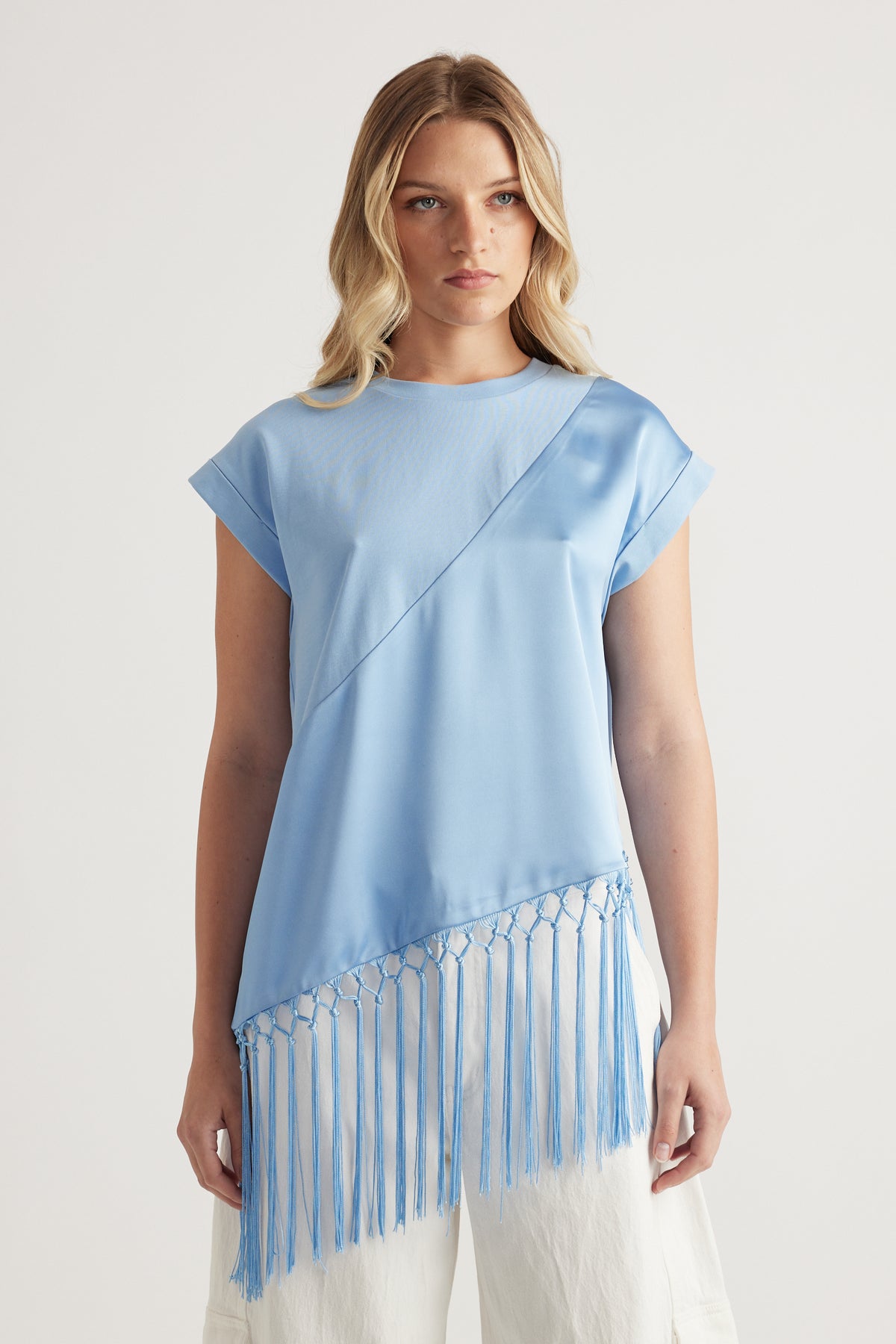 Woman wearing a light blue satin tee with an asymmetric fringe hem and white pants