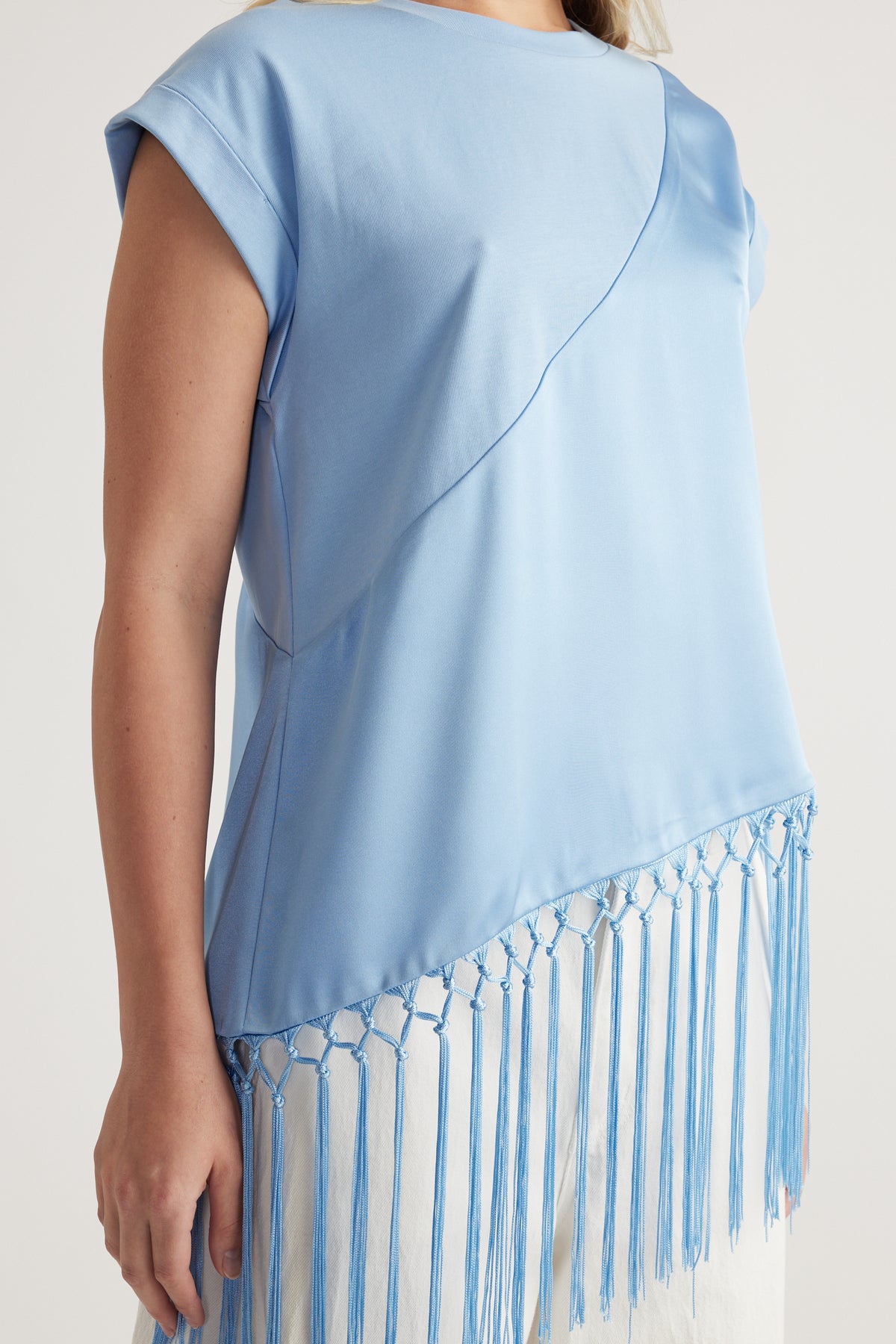 Woman wearing a light blue satin tee with short sleeves and an asymmetric fringe hem