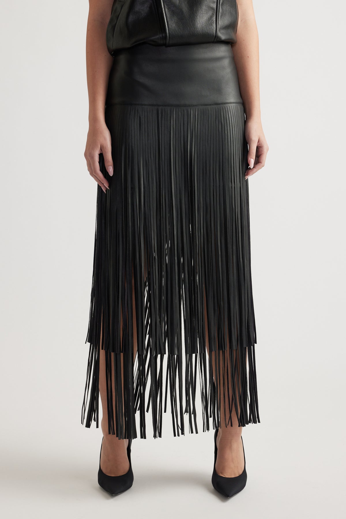 Front view of a fitted high-waist black skirt with tiered fringe detailing paired with black pointed heels