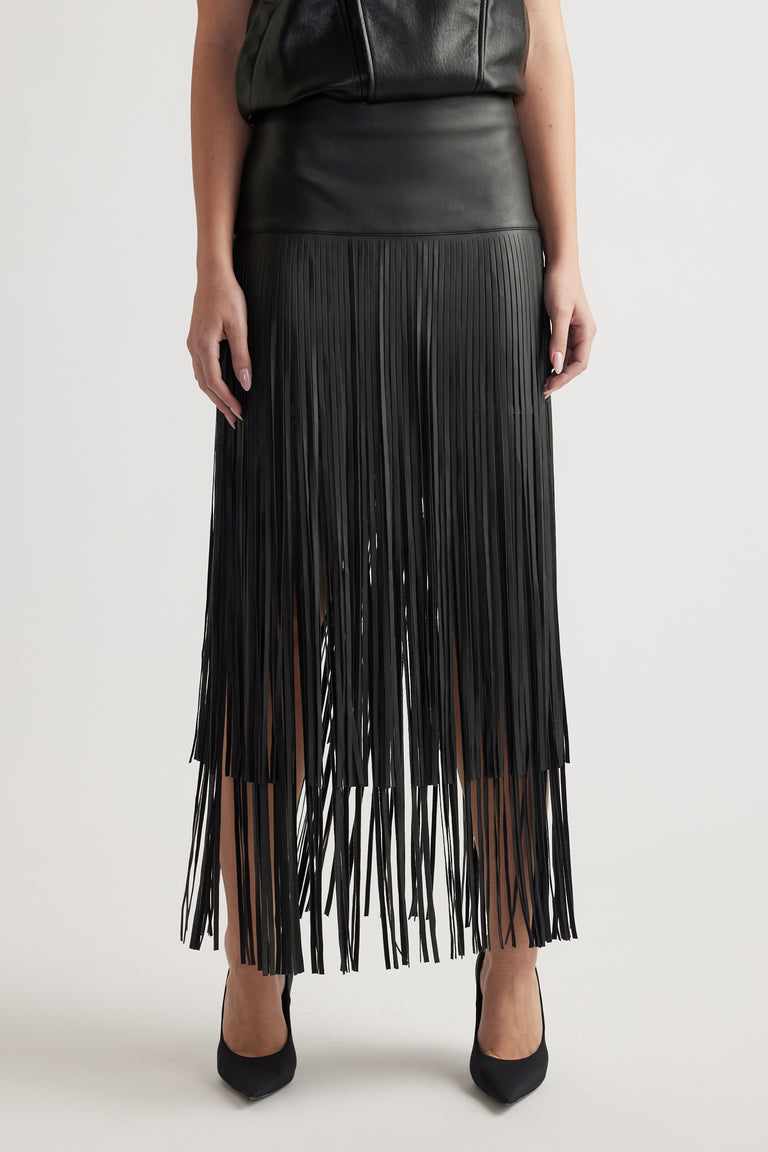 Front view of a fitted high-waist black skirt with tiered fringe detailing paired with black pointed heels