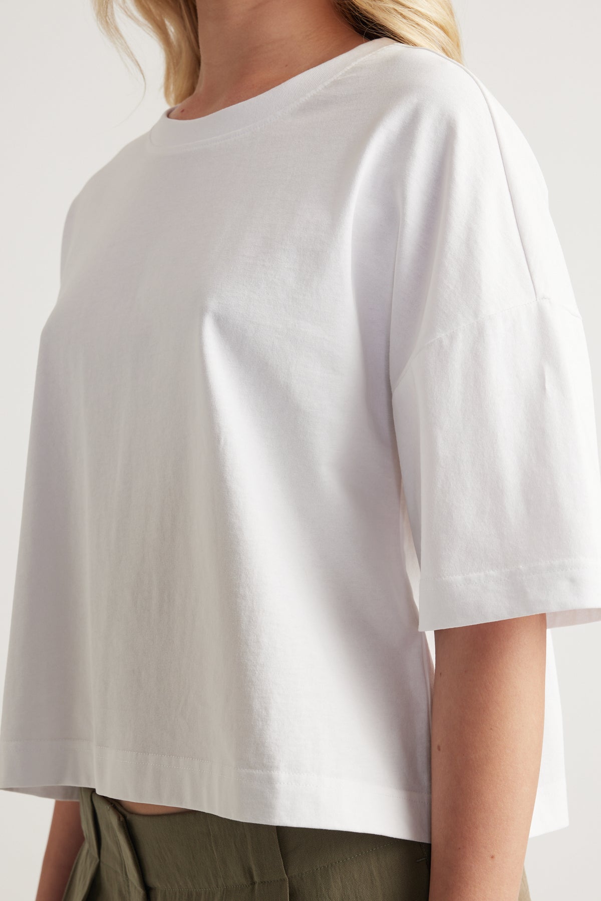 Woman wearing a white cropped boxy crew neck tee with relaxed short sleeves and olive pants