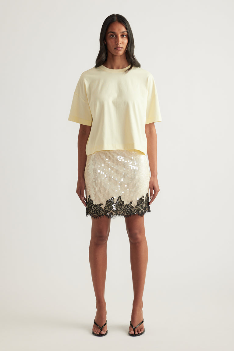 Woman wearing a cream cropped boxy tee with a sequin mini skirt featuring a lace hem and strappy sandals