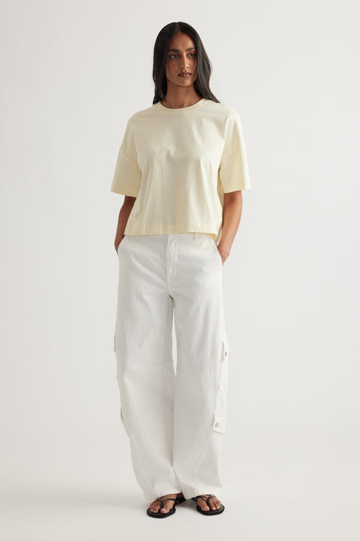 Woman wearing a cream cropped tee with white cargo pants and black sandals