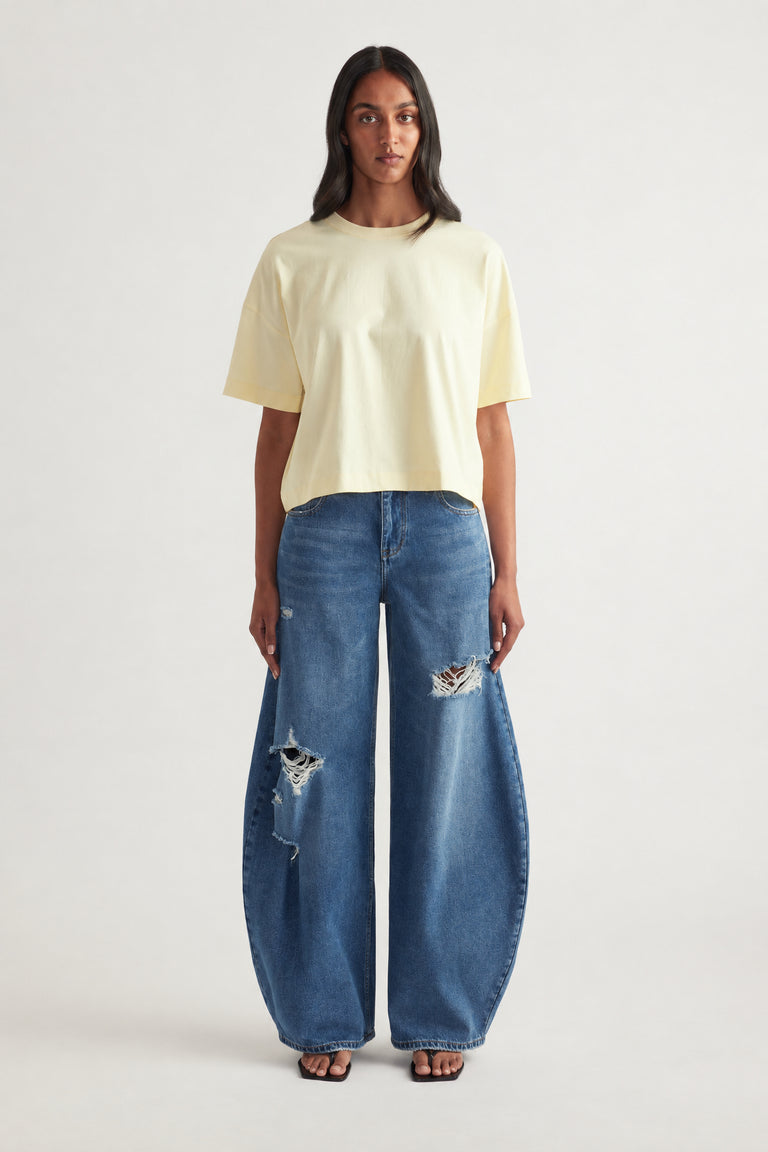 Woman wearing a pale yellow cropped tee with wide leg distressed blue jeans
