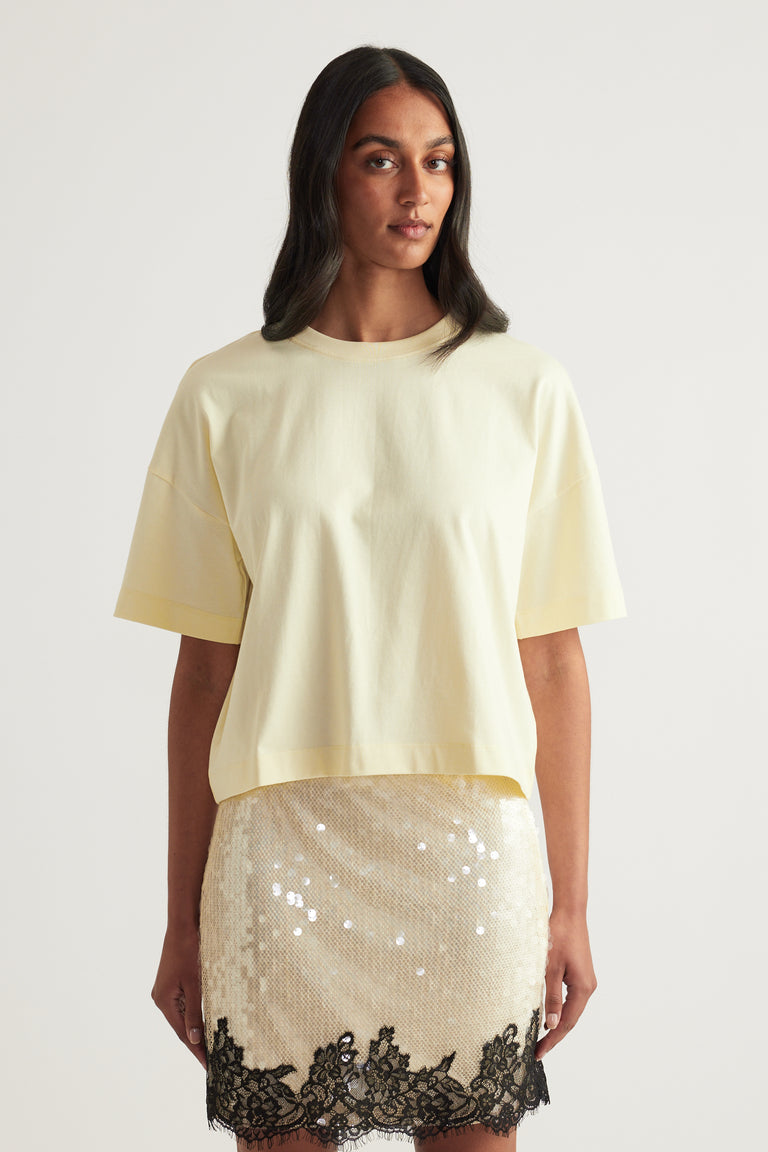 Woman wearing a pale yellow cropped boxy tee with a sequin skirt and black lace trim