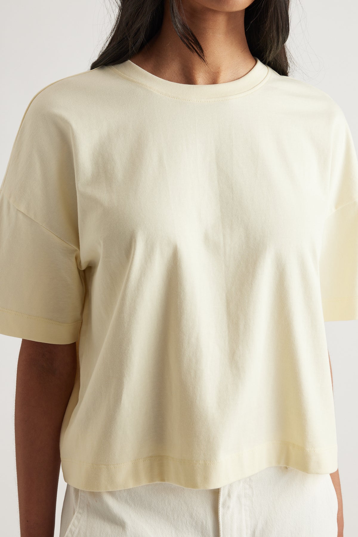 Woman wearing a cream cropped boxy tee with a crew neck and short sleeves