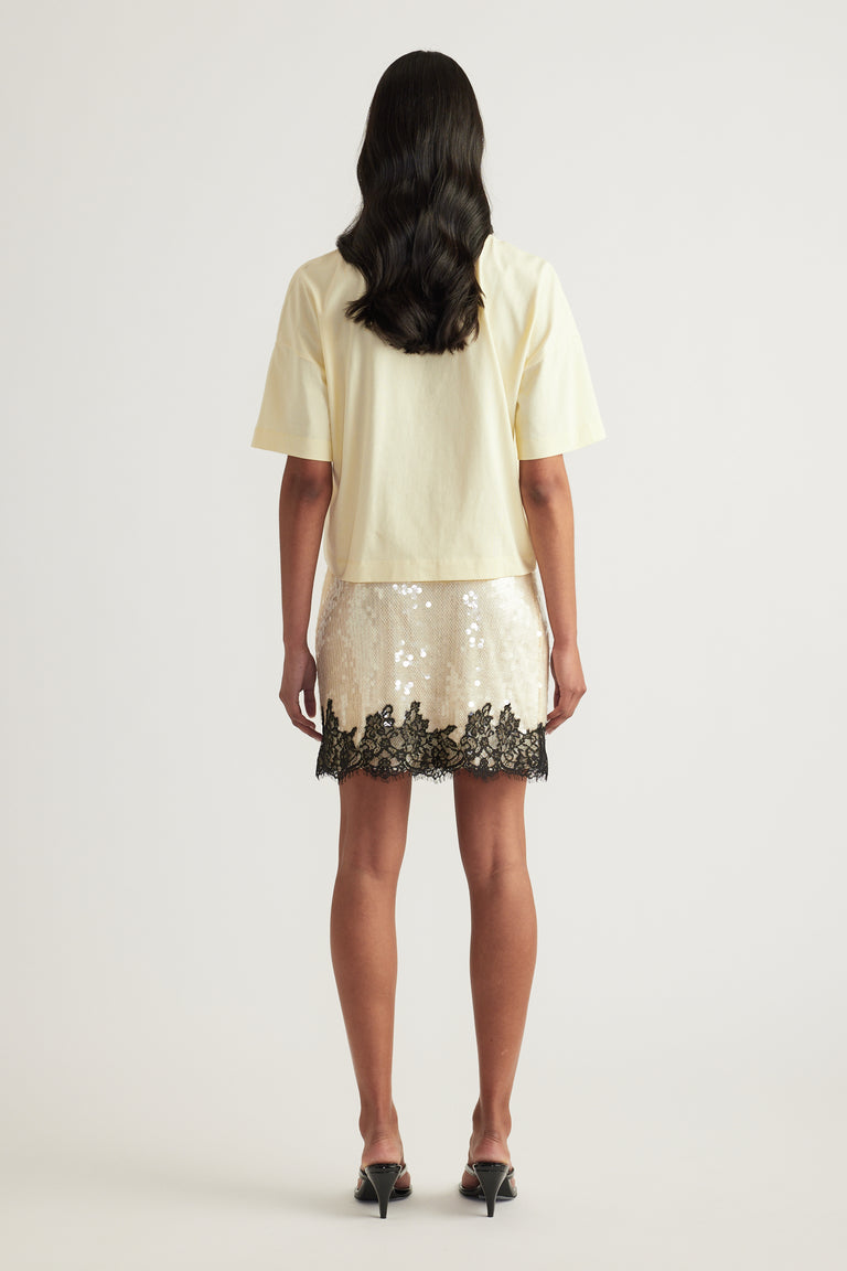 Back view of a woman in a cream cropped tee and sequin mini skirt with lace trim and black heels