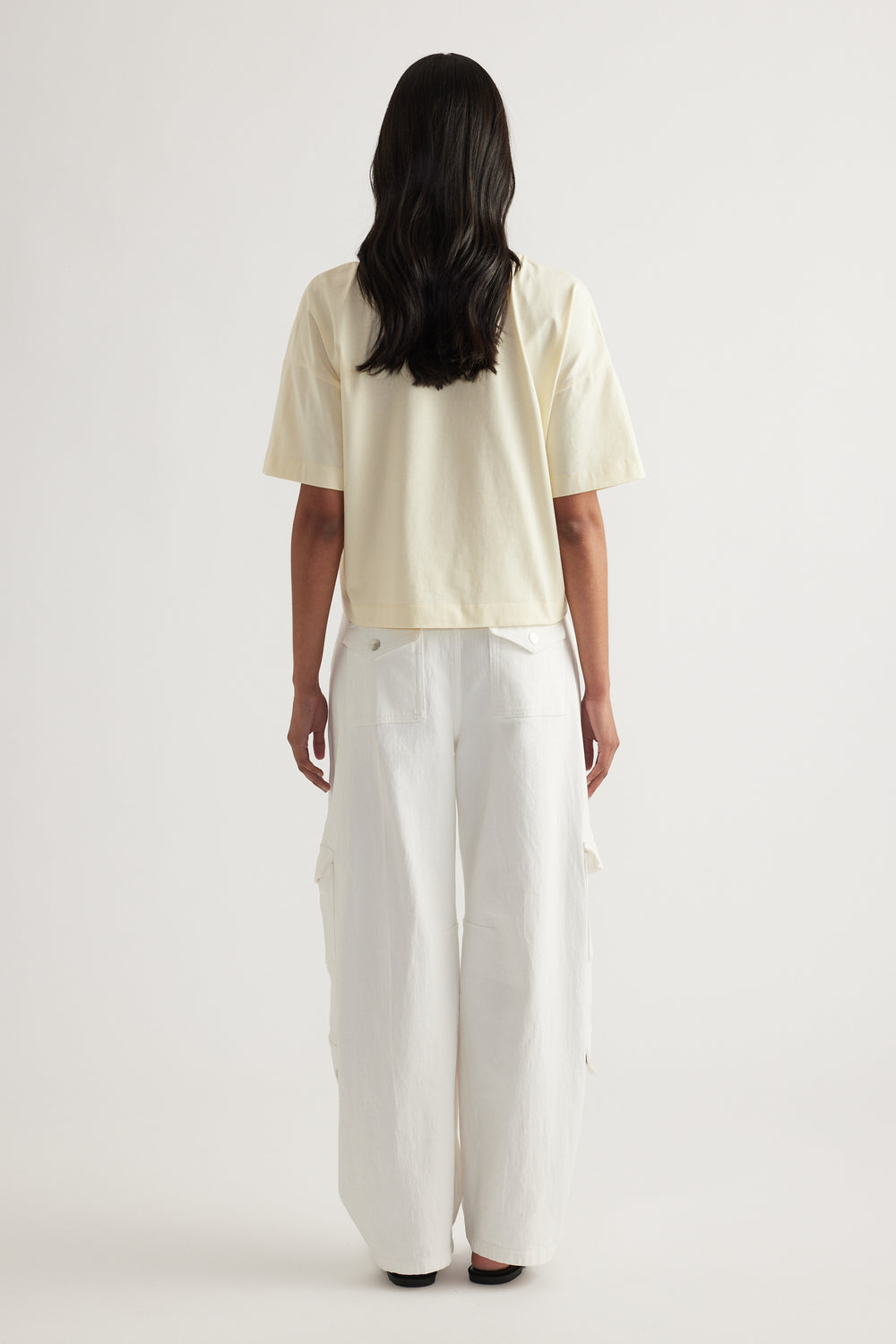 Back view of a woman wearing a cream cropped tee with white wide leg pants
