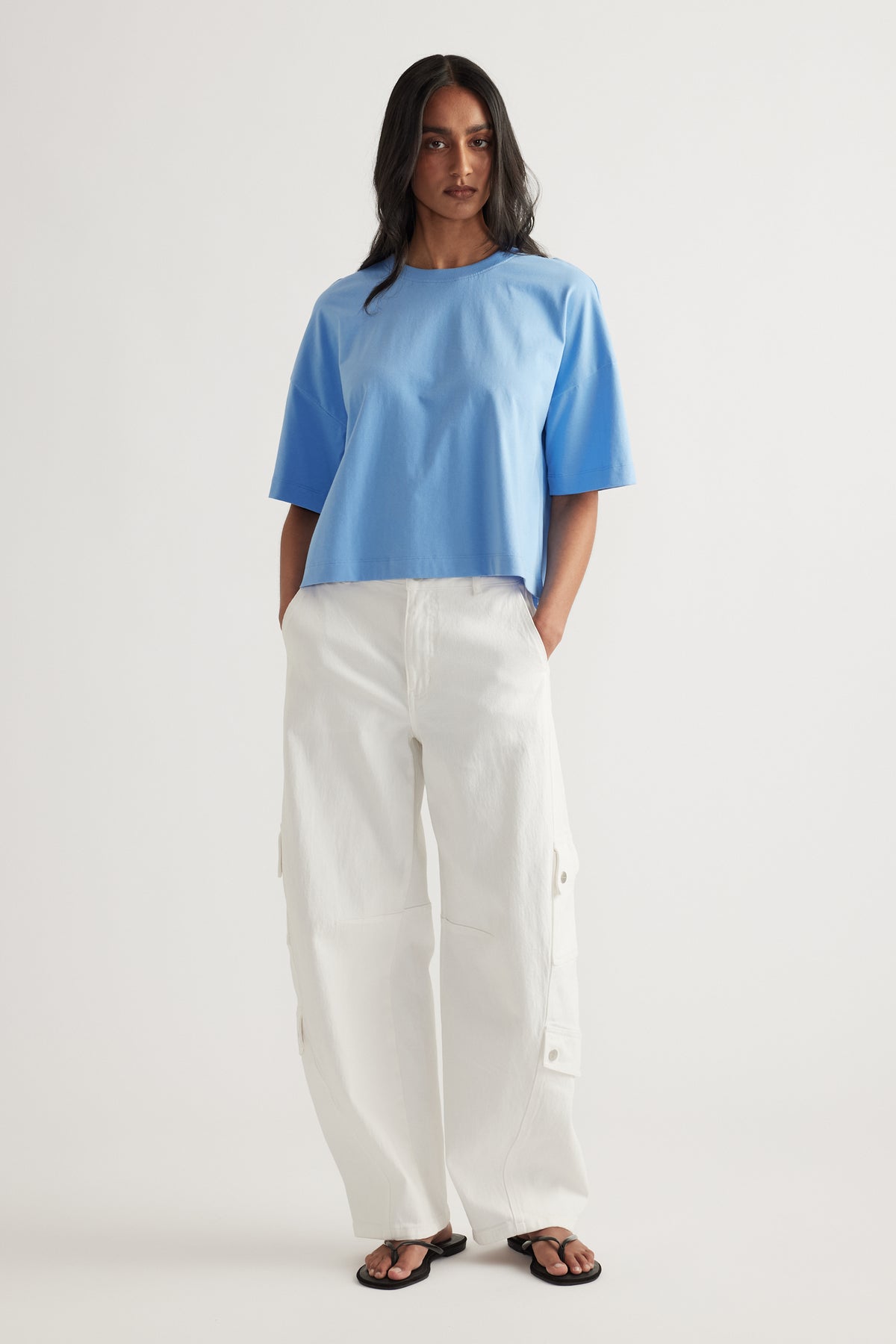 Model wearing a cropped blue boxy tee with white cargo pants and black sandals