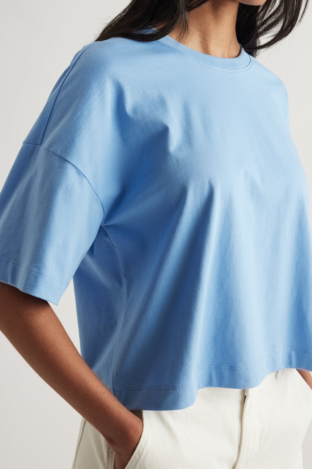 Woman wearing a light blue cropped boxy tee with short sleeves and white pants
