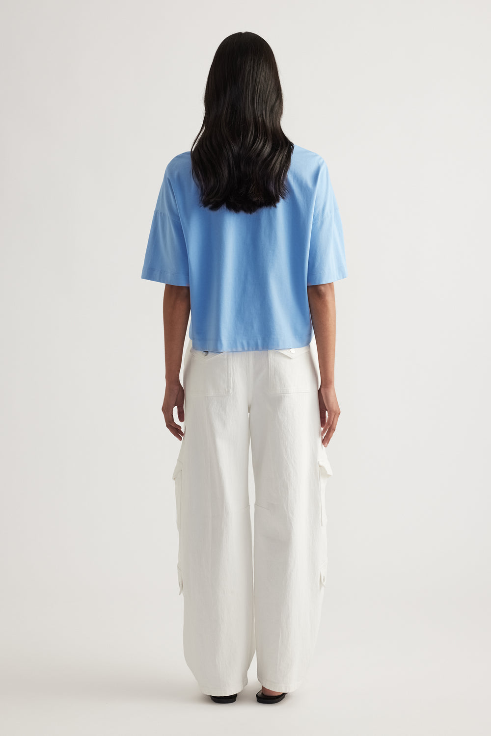 Back view of woman wearing a blue cropped tee with white wide leg cargo pants