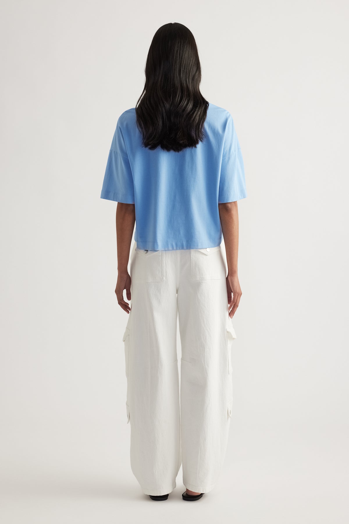 Back view of woman wearing a blue cropped tee with white wide leg cargo pants