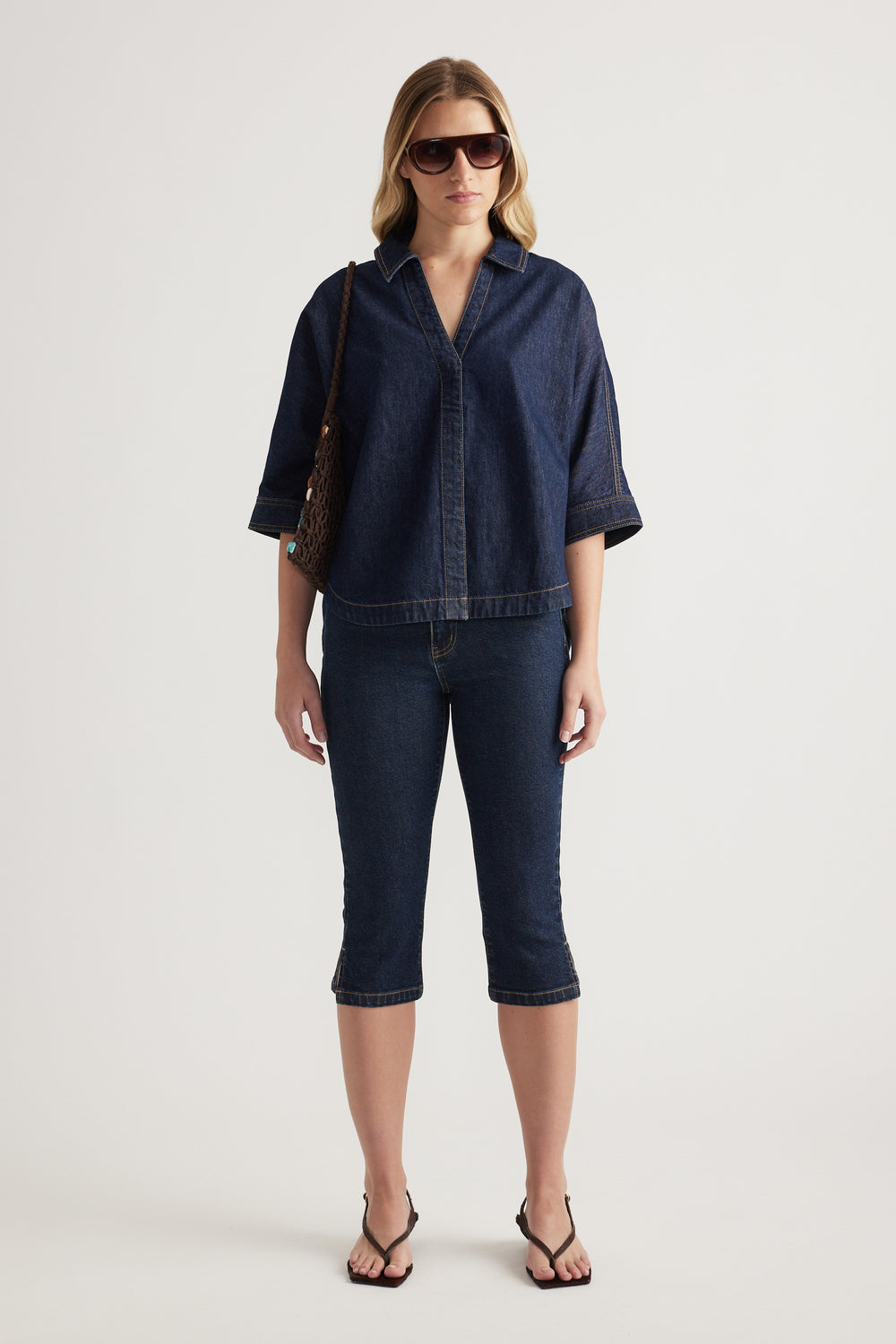 Woman in a dark denim collared shirt with elbow-length sleeves, matching cropped jeans and sandals