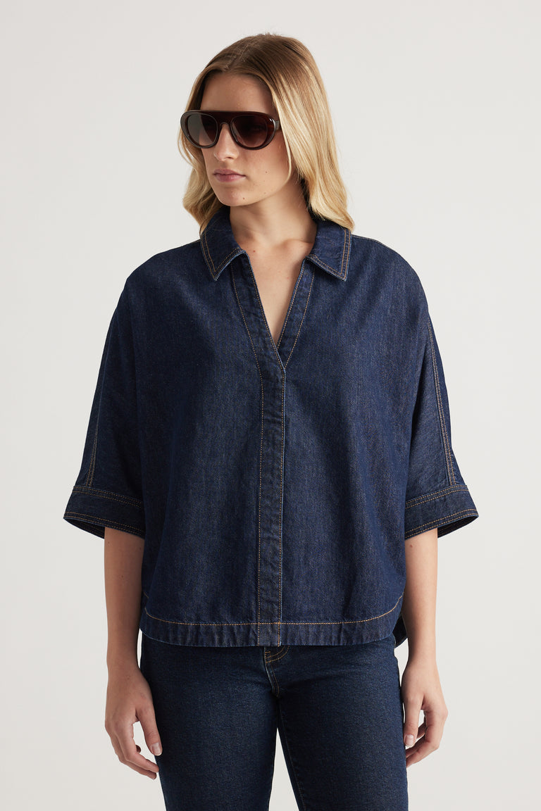 Woman wearing a dark denim shirt with elbow-length cuffed sleeves, collared V neckline and scooped hem