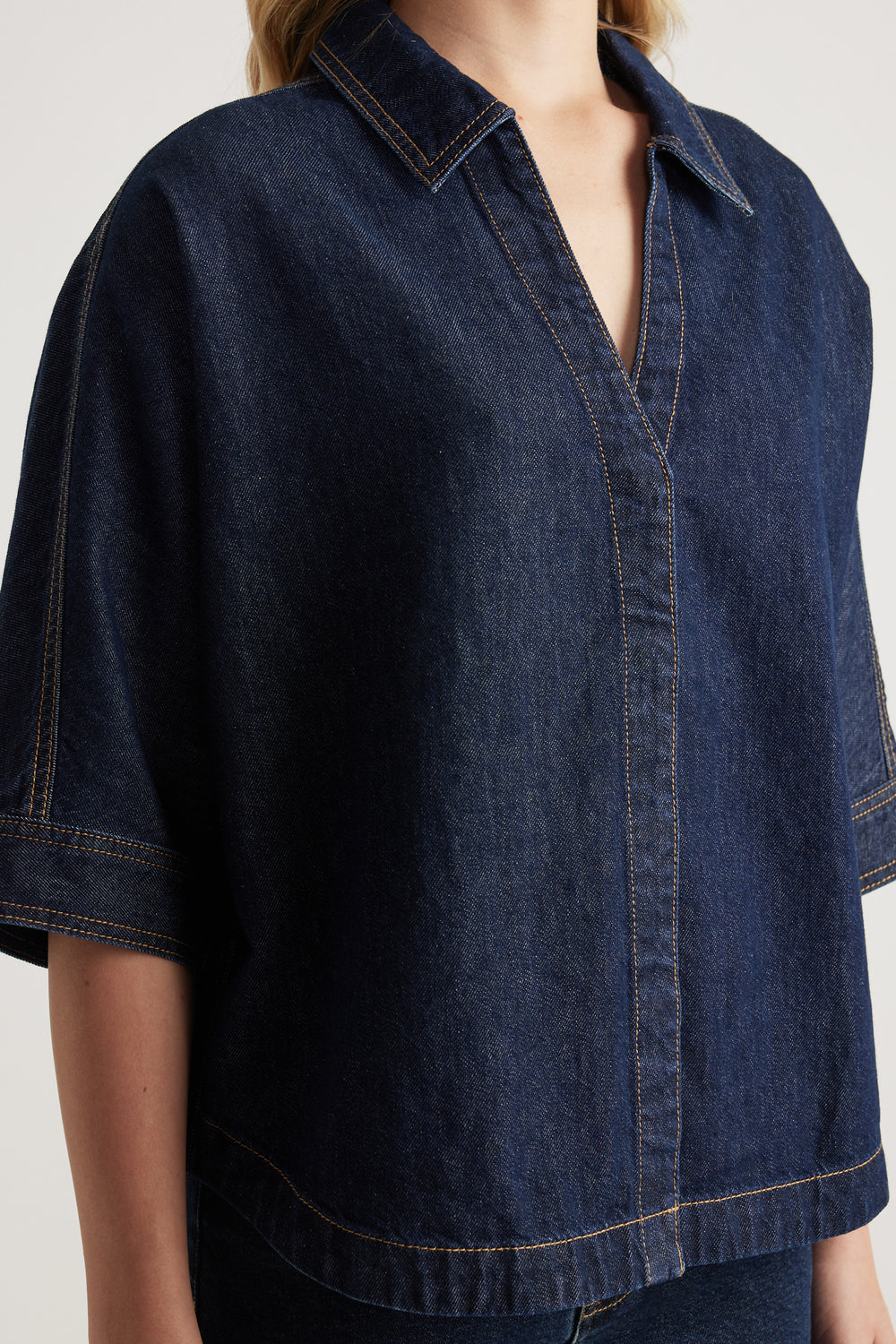 Woman wearing a dark denim shirt with a collared V neckline, elbow-length cuffed sleeves and scooped hem