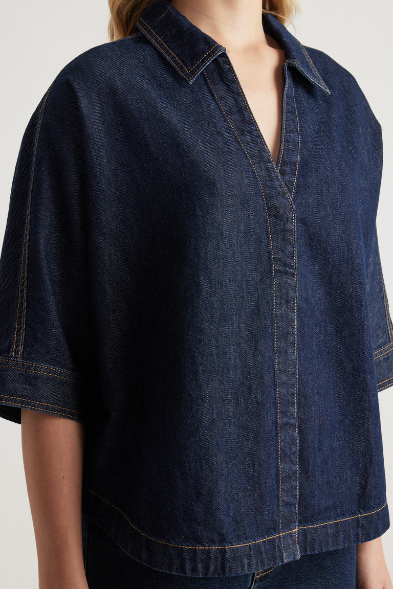 Woman wearing a dark denim shirt with a collared V neckline, elbow-length cuffed sleeves and scooped hem