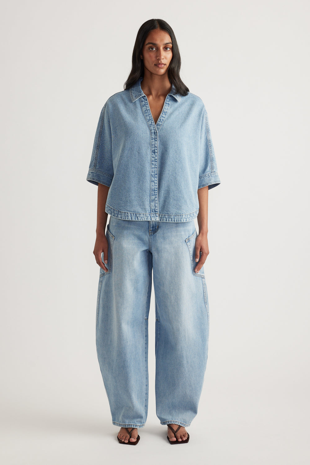 Woman wearing a light wash denim shirt with elbow-length sleeves and matching relaxed jeans