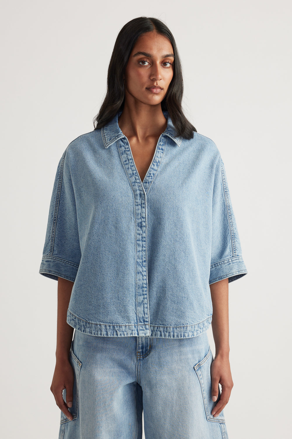 Woman wearing a light blue denim shirt with cuffed elbow-length sleeves and matching jeans