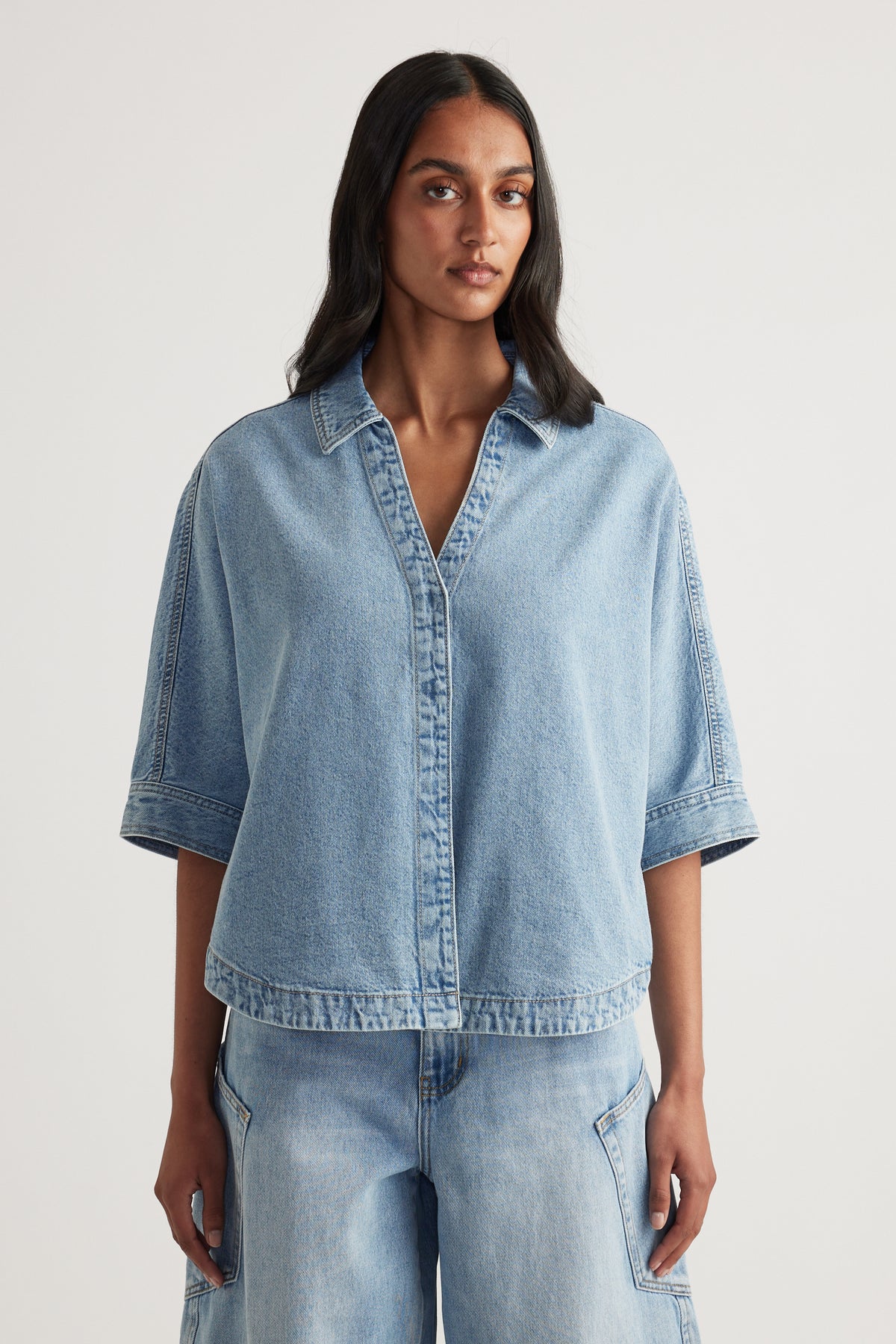 Woman wearing a light blue denim shirt with cuffed elbow-length sleeves and matching jeans