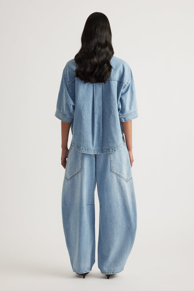 Back view of a woman wearing a light wash denim shirt with cuffed sleeves and matching wide leg jeans