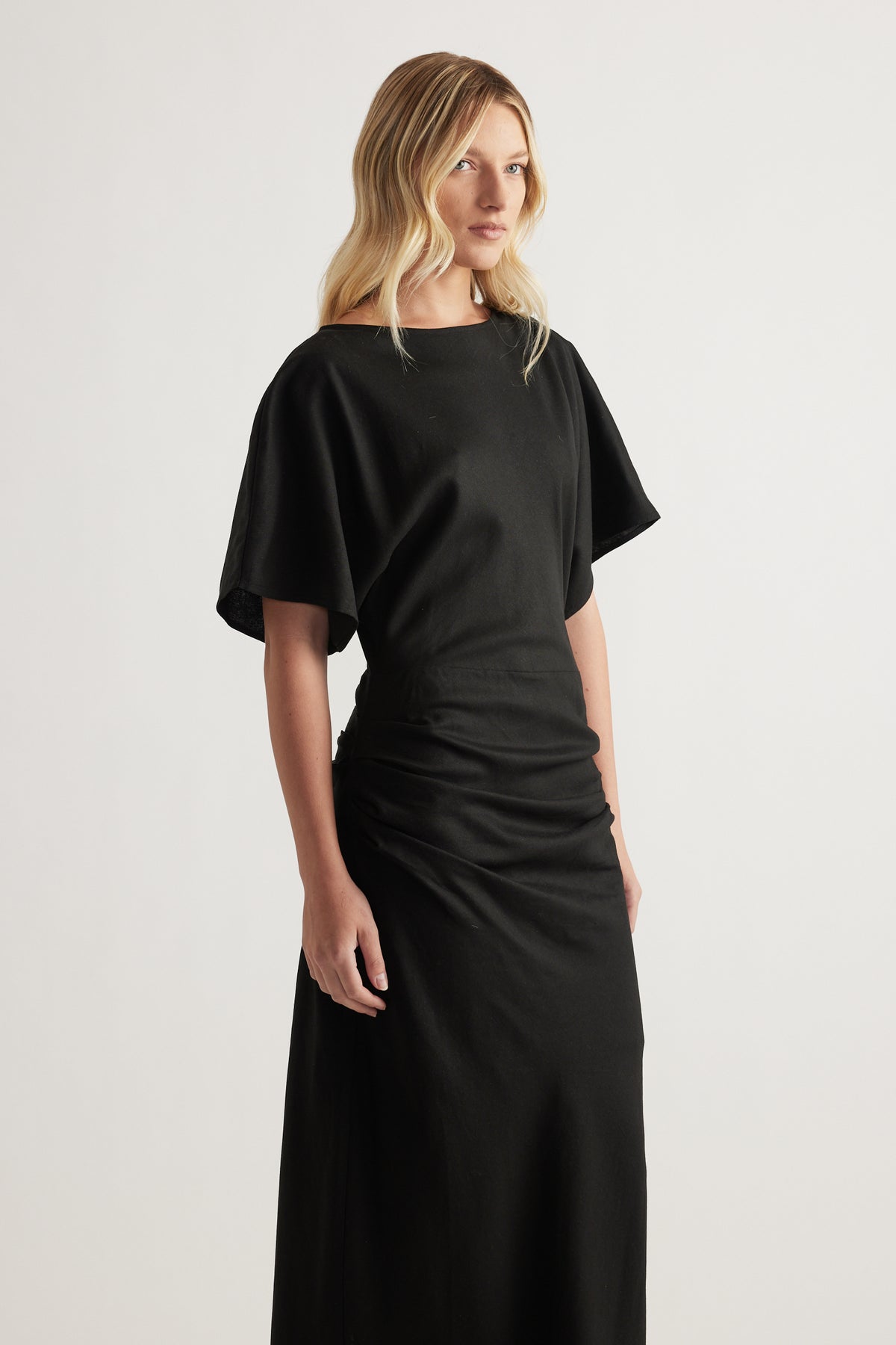 Woman wearing a black boat neck dress with short sleeves and ruched side detail