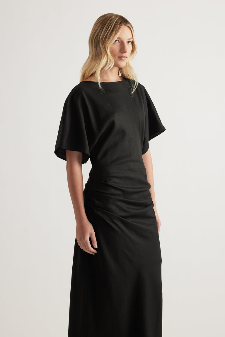 Woman wearing a black boat neck dress with short sleeves and ruched side detail