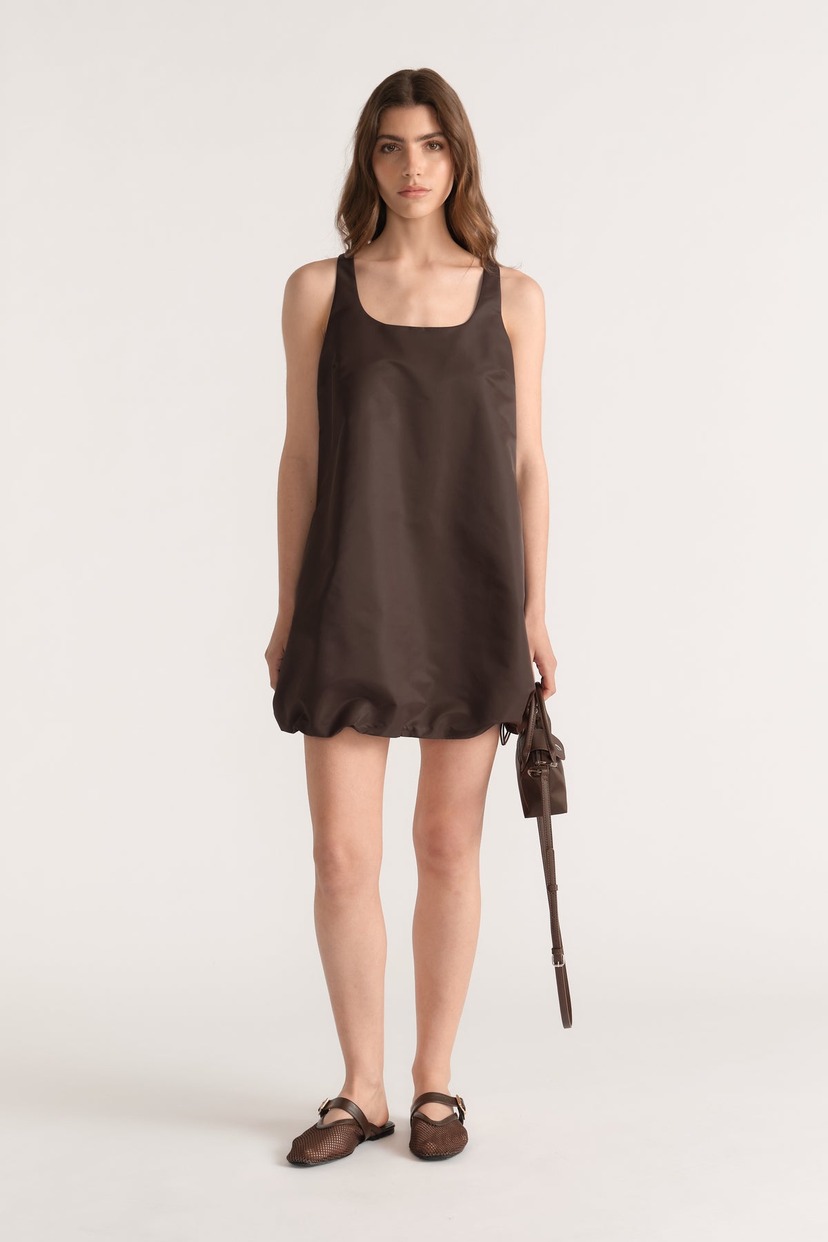 Model wearing a brown sleeveless scoop neck bubble mini dress with a drawcord hem and side pockets