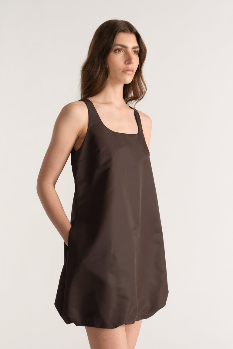 Woman wearing a brown sleeveless bubble mini dress with a scoop neckline and side pockets