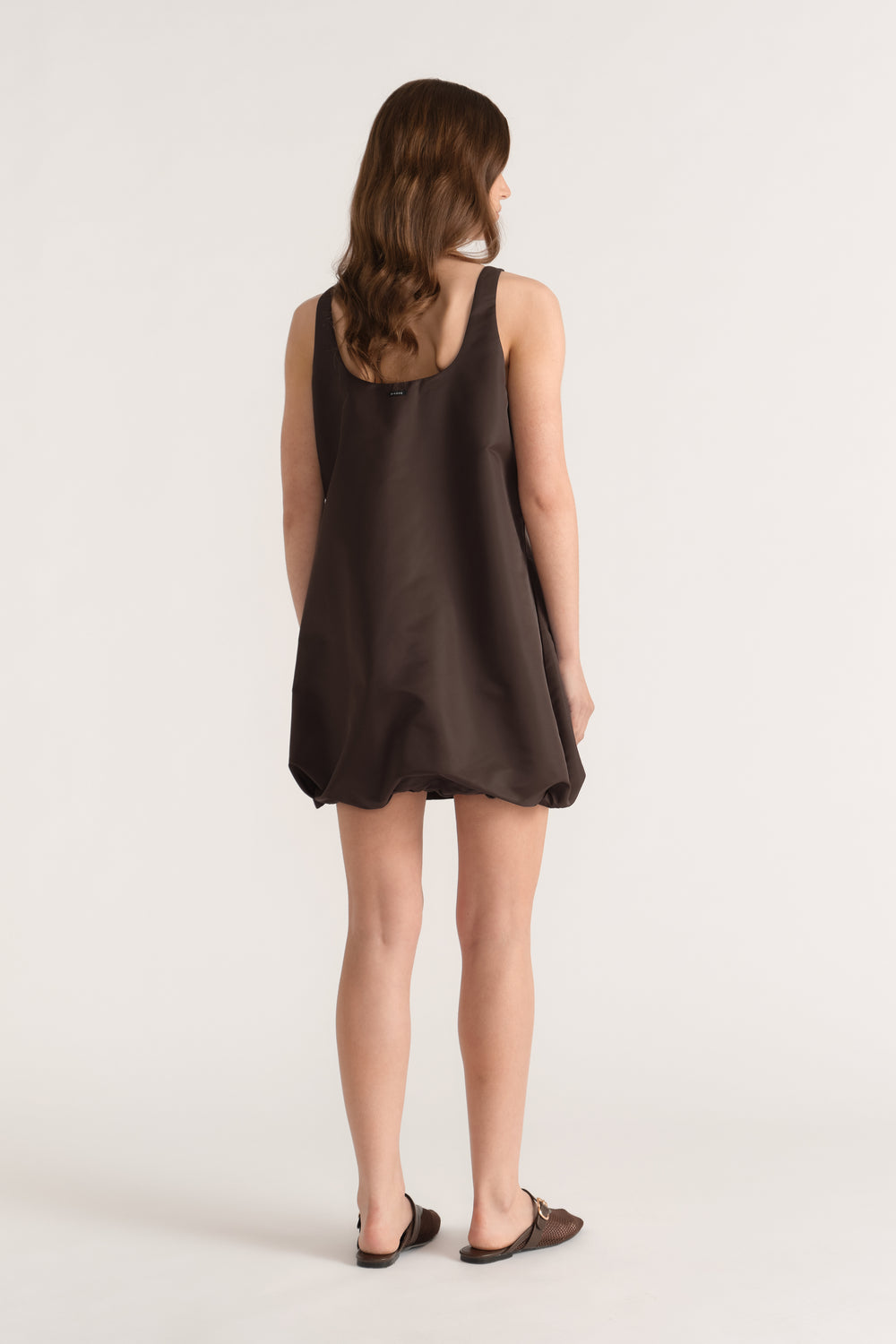 Woman viewed from behind in a dark brown sleeveless bubble mini dress with a scooped neckline